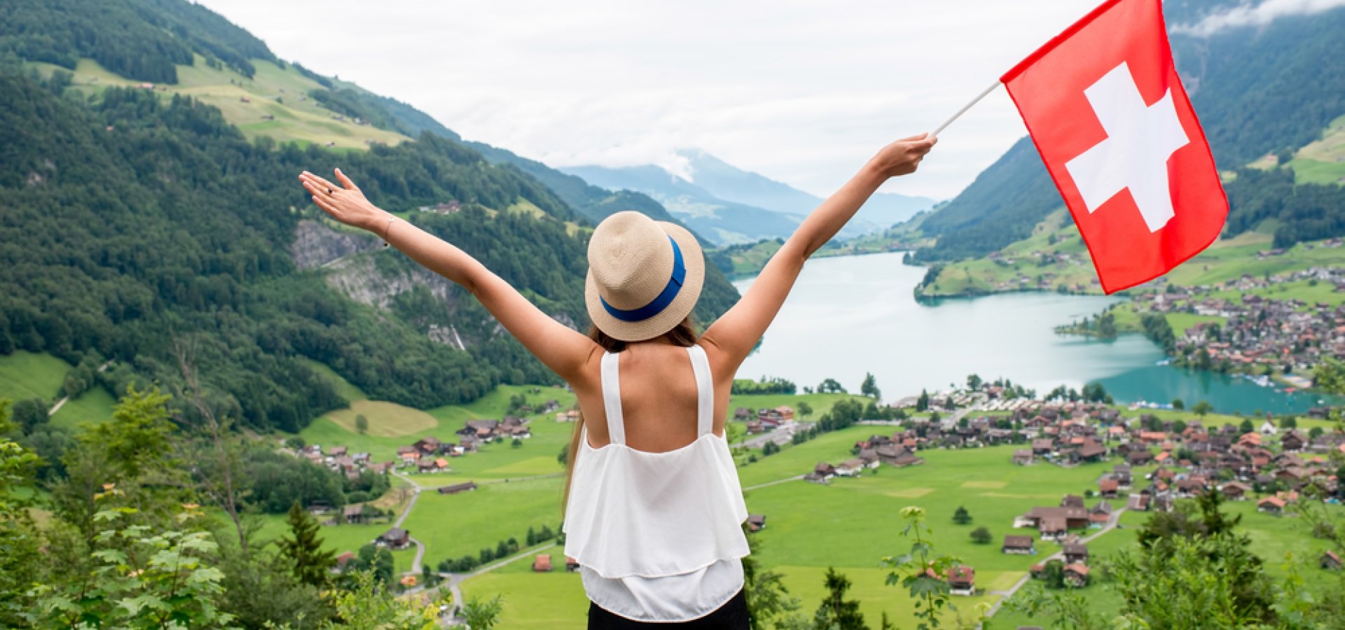 Young woman with swiss flag enjoying great landscape view on the valley with lake and village in Switzerland.